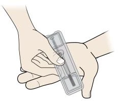Two hands holding and preparing a transparent rectangular medical device containing a syringe with an internal needle