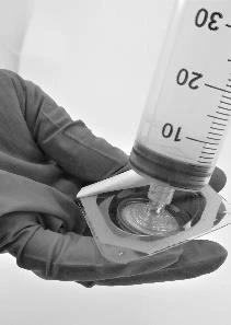 Una mano guantata tiene un flaconcino di vetro mentre aspira il liquido con una siringa graduata in bianco e nero