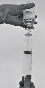 Una mano guantata tiene un flacon con liquido mentre l'altra mano impugna una siringa collegata per il prelievo del farmaco
