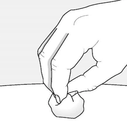 Una mano tiene tra pollice e indice un piccolo oggetto bianco e arrotondato sopra una superficie piana