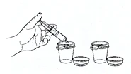 A hand holds a syringe to aspirate the contents from a glass vial, next to a second vial and their respective caps.