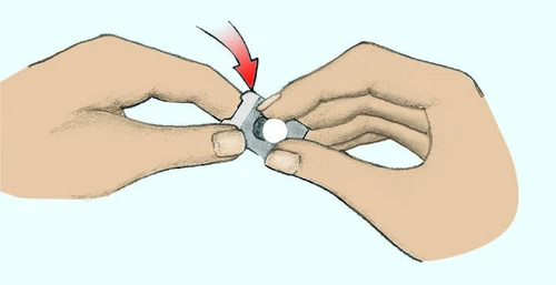 Due mani tengono e premono un dispositivo medico con un pulsante bianco centrale indicato da una freccia rossa verso il basso