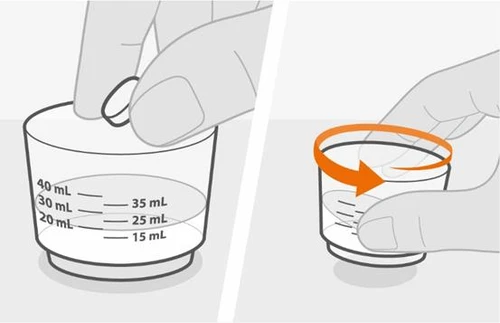 A hand holding a graduated measuring cup with milliliter markings and a