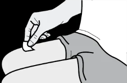 Una mano applica un piccolo cerotto bianco sulla pelle della coscia di una persona seduta con indosso dei pantaloncini corti