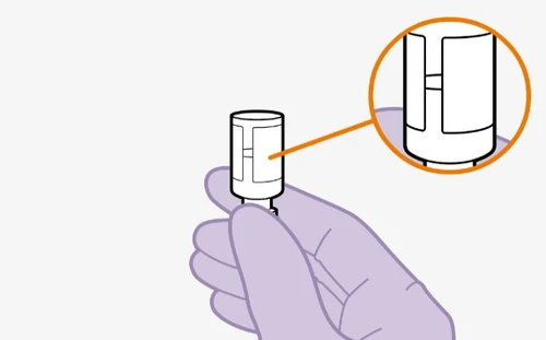 A hand holding a white cylindrical medical device with a circular magnification showing a detail of the top part