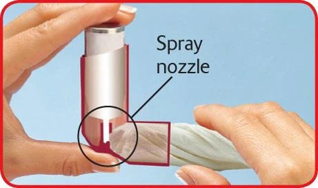 Dłonie trzymające biało-czerwony inhalator z zaznaczoną linią wskazującą na dyszę sprayu oraz okręgiem na dolną część urządzenia