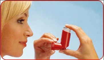 Perfil de una mujer rubia mirando hacia un lado, sosteniendo con ambas manos un inhalador rojo listo para su uso sobre un fondo azul claro