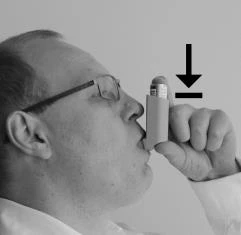 A man with glasses holds the inhaler to his mouth, with a black arrow indicating the direction of pressing the device during inhalation