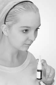 A young woman with light hair and a headband attentively looking at a small bottle with eye drops which she holds in her hand in front of her