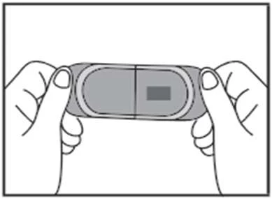 Two hands holding horizontally a gray rectangular medication or medical device with a darker rectangle visible on the right side