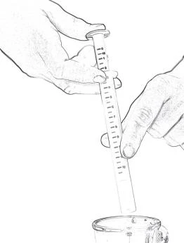Two hands holding a syringe vertically with a millimeter scale, the tip of which is submerged in a glass container filled with liquid