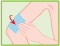 Mano che applica un cerotto blu sul braccio flesso, con freccia rossa che indica la direzione di adesione del materiale alla pelle
