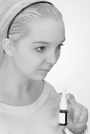 A young woman with light hair and a headband looks down at a small dropper bottle with a pipette in her hand, against a white background