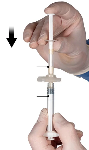 Manos con guantes blancos sosteniendo una jeringa con líquido transparente, flechas negras indican la dirección del movimiento del émbolo y el nivel del medicamento