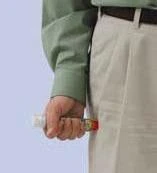 A hand holding a small vial with a red label on a light blue background, person wearing a green shirt and light-colored pants