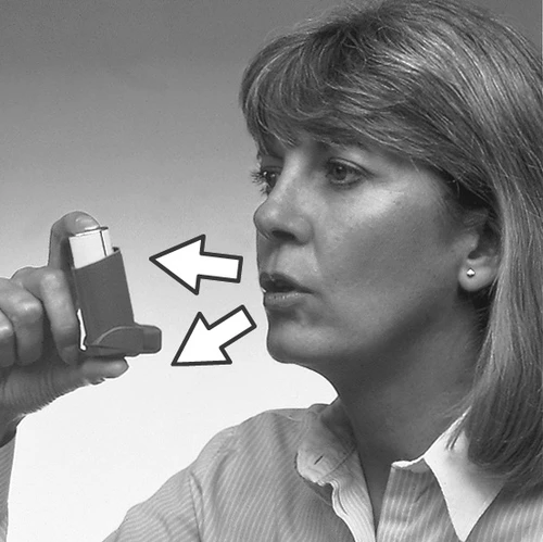 A woman holding the inhaler close to her mouth; two white arrows indicate the correct way of holding the device and the direction of inhalation by the patient