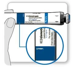 Hand holding a white vial of Genotropin 5.3 mg/ml, with a magnified inset showing a close-up of the label marked LOT and EXP