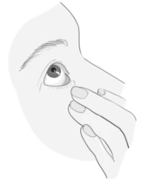 Primer plano del ojo y la nariz humanos, mientras una mano toca suavemente el rabillo del ojo con el dedo índice y medio para la aplicación del medicamento