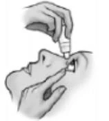 Hands holding a small bottle and an applicator, administering drug drops directly into the eye of a person with a slightly tilted head in profile