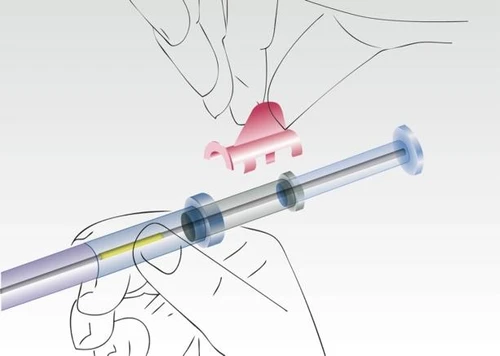 Mano sosteniendo una jeringa transparente con líquido amarillo, colocando una tapa rosa en su extremo durante el proceso de preparación del medicamento
