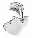 A hand holds a small bottle and applies drops directly into the open eye of a person looking upward, shown in profile