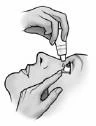 A hand holding a small bottle and applying drops to a person's eye while another hand gently pulls down the user's lower eyelid