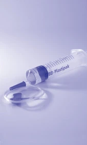 Una jeringa transparente con la inscripción BD Plastipak colocada junto a una aguja desacoplada sobre un fondo claro azulado