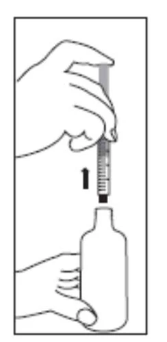 A hand holding a syringe vertically above a medication vial, preparing to draw liquid from the container using the needle