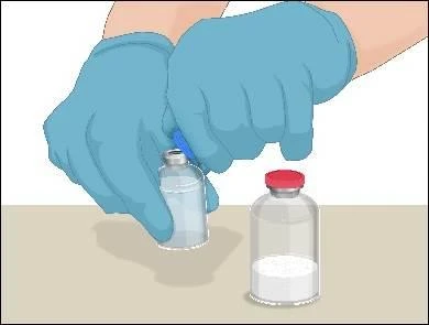 Hands wearing blue medical gloves holding a glass vial with liquid over another empty vial with a red stopper against a light background