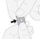 Hands holding a small, gray square patch with a hole in the center, indicated by a black arrow pointing to the right