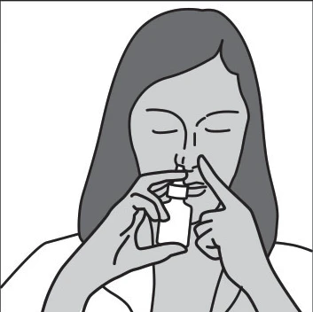 Donna con gli occhi chiusi tiene un piccolo flacone vicino al naso, utilizza un dito per applicare il farmaco dall'erogatore direttamente nella narice
