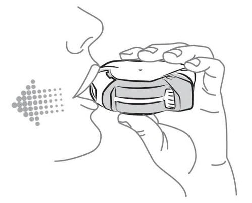 Profile view of a person holding an inhaler with hands at the mouth, a dotted arrow indicating the direction of medication being blown into the oral cavity