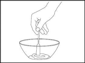 A hand holding a small spoon stirring the liquid contents inside a glass bowl