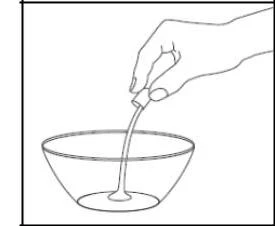 A hand holding a small package from which a thick, light-colored liquid substance flows into a glass bowl