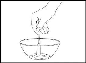 A hand holding a small spatula mixing a white substance inside a transparent bowl on a light background
