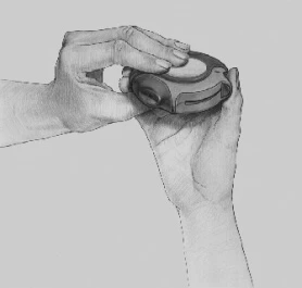 Dwie dłonie trzymają i obracają okrągły, ciemny dozownik z białym przyciskiem na górze w celu przygotowania leku do użycia