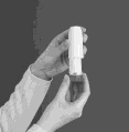 Two hands holding a white, cylindrical medical inhaler vertically against a uniform dark gray background