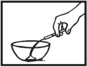 Hand holding a small container or pipette, from which liquid flows directly into a white bowl placed below