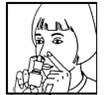 A woman administering a nasal spray into her nose, holding the bottle in one hand and supporting her nose with the other, head slightly tilted forward