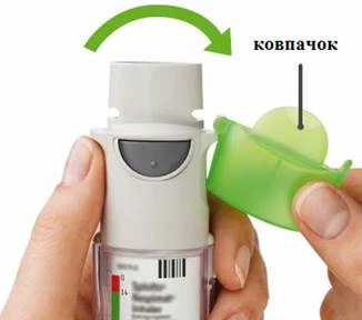 Mano che impugna un inalatore, l'altra mano apre il tappo verde, una freccia indica il senso di rotazione per l'apertura